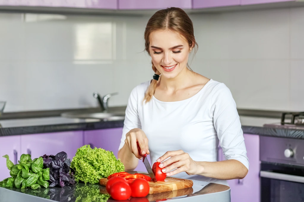 Sarah Miller smiling as she focuses on chopping a fresh red tomato on a wooden cutting board for a new recipe.