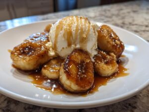 Close-up of caramelized bananas foster slices topped with a scoop of vanilla ice cream and caramel sauce.