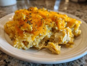 A close-up serving of cheesy chicken and rice casserole topped with melted cheddar and dried herbs.
