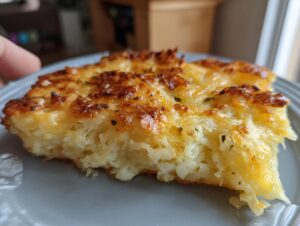Close-up of a thick, creamy slice of hashbrown casserole with a golden, bubbly cheese crust.