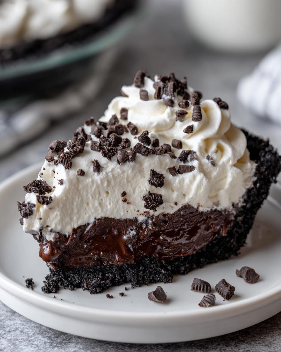 A decadent slice of Christmas chocolate cream pie featuring a dark crust, rich filling, and thick whipped cream topped with chocolate crumbles.