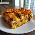 A hearty slice of Dorito Casserole featuring ground beef, melted cheese, and a crunchy Dorito topping on a white plate.