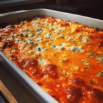 Close-up of hot, bubbling Buffalo chicken dip topped with melted orange cheese and crumbles of blue cheese.