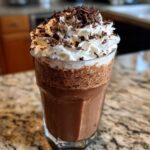 A tall glass of rich, blended frozen hot chocolate topped with whipped cream and chocolate shavings.
