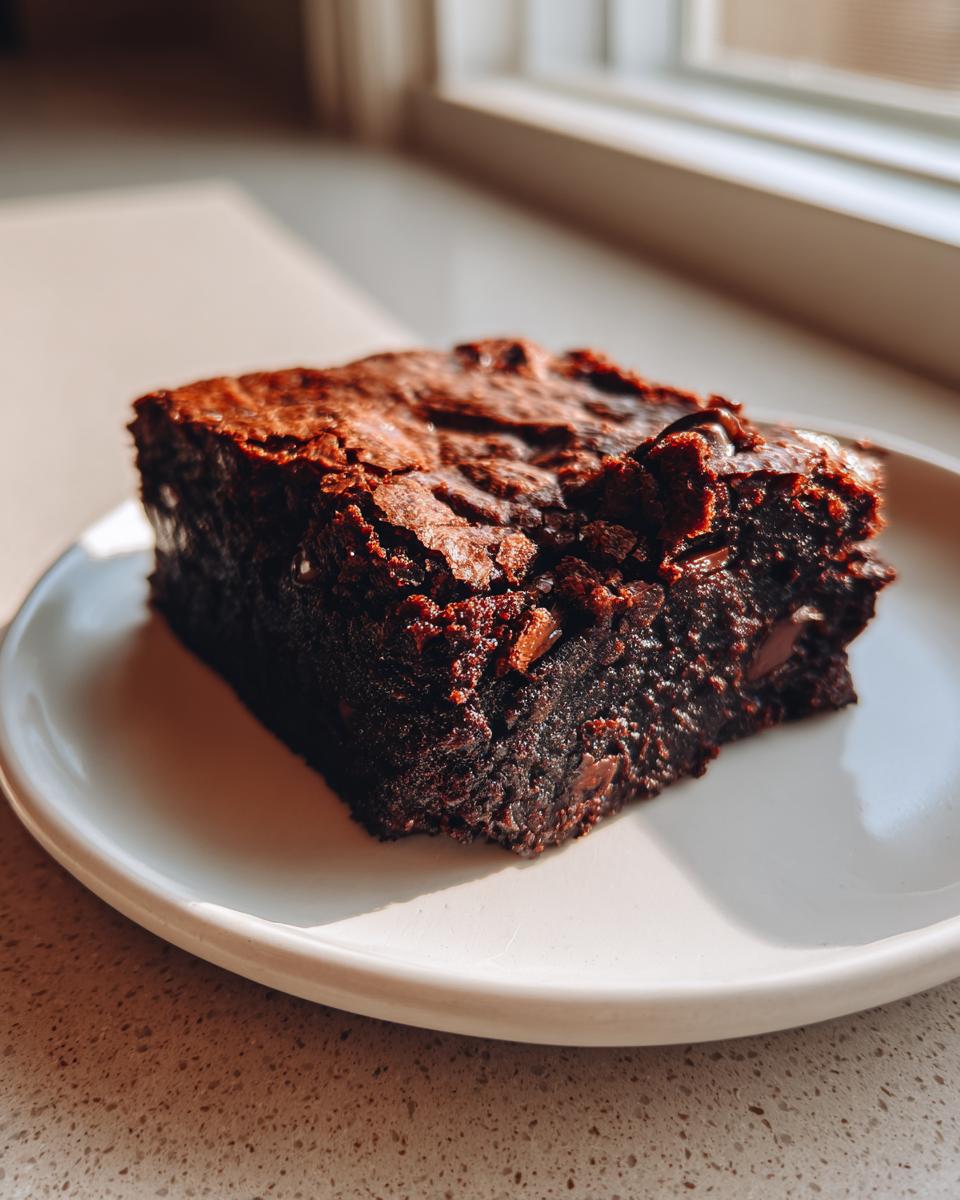 A single, fudgy square of rich dark chocolate sweet potato brownies on a white plate.