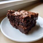 Two rich, fudgy sweet potato brownies stacked on a white plate, showing a shiny, cracked top.