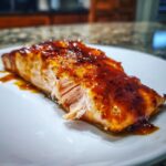 Close-up of a perfectly cooked salmon fillet topped with a thick, glossy, dark orange glaze.