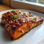 Close-up of a perfectly cooked piece of teriyaki salmon, heavily glazed and topped with sesame seeds and chopped green onions.