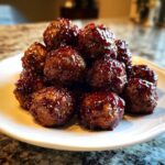 A mound of shiny, glazed Grape Jelly Meatballs piled high on a white serving plate.