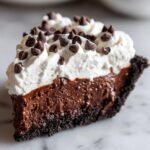 A decadent slice of Christmas chocolate cream pie featuring a dark crust, rich chocolate filling, and whipped cream topped with mini chocolate chips.