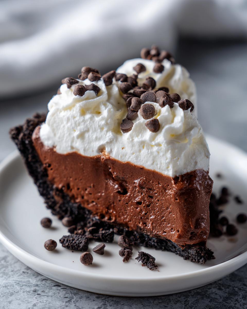 A rich slice of Christmas chocolate cream pie featuring a dark crust, thick chocolate filling, and whipped cream topped with mini chocolate chips.