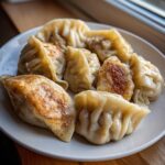 A plate filled with freshly cooked Traditional Chinese Dumplings, some steamed and some pan-fried golden brown.