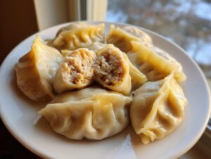 A plate of freshly steamed Traditional Chinese Dumplings, one cut open to show the savory meat filling inside.