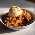 A warm serving of homemade apple crisp topped with a melting scoop of vanilla ice cream.