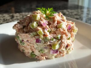 A molded serving of creamy salmon salad mixed with celery, red onion, and peas, garnished with parsley.