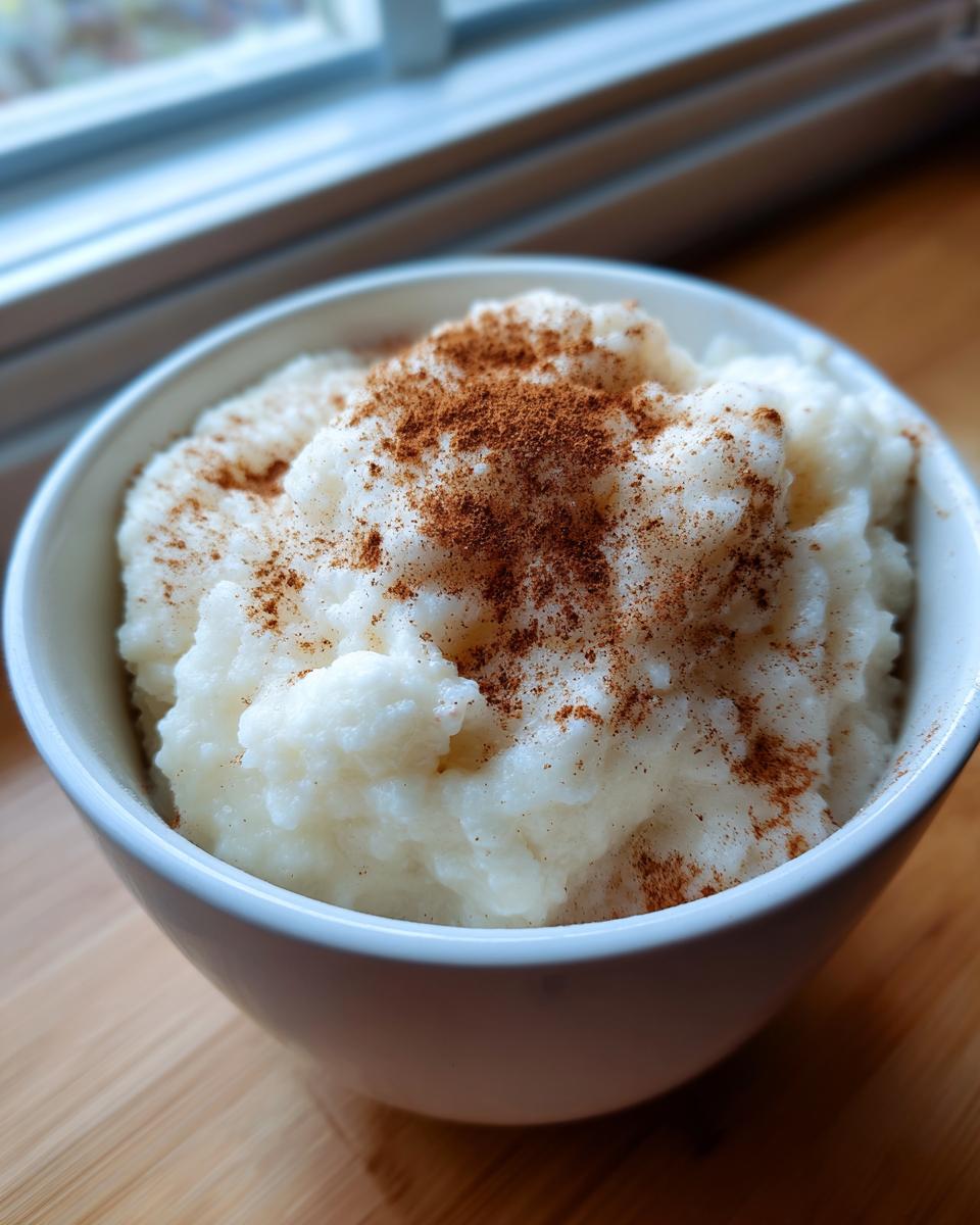 A close-up of creamy white rice pudding recipe topped generously with ground cinnamon in a white bowl.