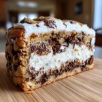 Cross-section of a layered chocolate chip cookie cake recipe with creamy white filling and melted chocolate chunks.