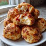 A stack of golden-brown pizza bites, with the top ones broken open revealing gooey, melted cheese and pepperoni inside.