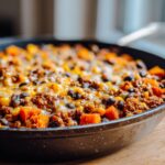 Close-up of a hearty sweet potato skillet topped with melted cheese, black beans, corn, and seasoned ground meat.