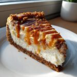 A perfect slice of baked salted caramel cheesecake featuring a thick graham cracker crust and rich caramel drizzle.
