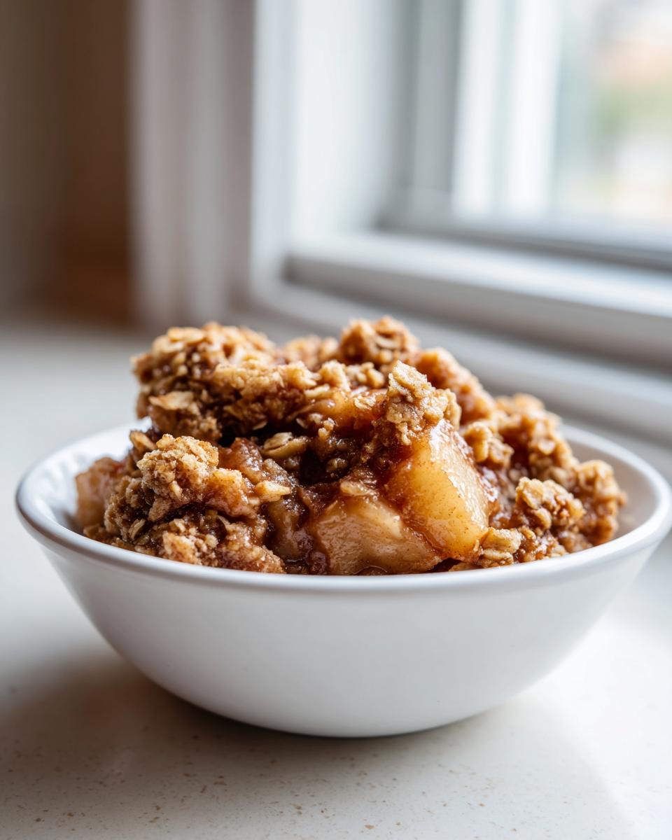 A close-up of a serving of the best apple crisp recipe, featuring warm, spiced apples and a crunchy oat topping in a white bowl.