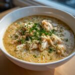 A close-up of a bowl of creamy crab soup generously topped with large chunks of white crab meat and chopped parsley.