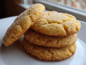A close-up stack of four golden brown butter sugar cookies coated in sparkling granulated sugar.