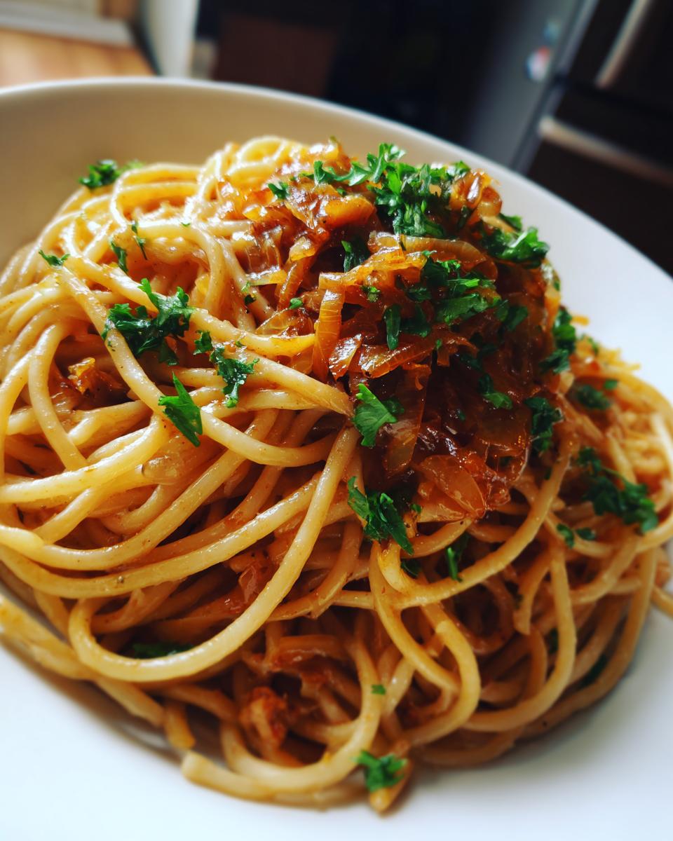 A close-up shot of a bowl of spaghetti tossed in sauce and topped generously with caramelized onion pasta and fresh parsley.