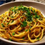 A close-up, appetizing photo of spaghetti tossed in rich sauce and topped with generous caramelized onion pasta and fresh parsley.