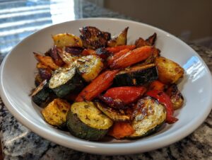 A white bowl filled with colorful, caramelized roasted vegetables including zucchini, carrots, and peppers.