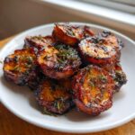 Close-up of caramelized, roasted sweet potatoes slices topped with fresh thyme.