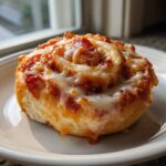 A freshly baked, single serving of pizza pinwheels topped with melted mozzarella cheese and pepperoni pieces.