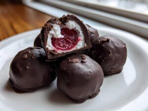 A stack of homemade chocolate covered cherries, one cut open revealing a cherry center and white filling.
