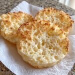 Three golden-brown, airy rounds of homemade cloud bread resting on a white paper towel.