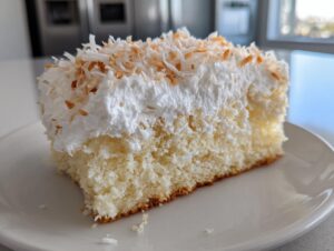 Close-up of a moist slice of coconut poke cake topped with whipped cream and toasted coconut flakes.