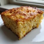 A close-up, appetizing slice of cream cheese corn casserole with a rich, golden-brown, slightly caramelized top.