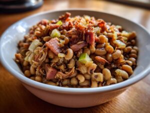Close-up of a white bowl filled with creamy black eyed peas topped with chunks of bacon and sautéed onions.