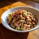 A bowl of creamy black eyed peas topped with shredded ham and chopped green celery.