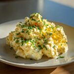 A generous serving of creamy egg salad recipe, garnished with freshly chopped green chives, presented on a light plate.