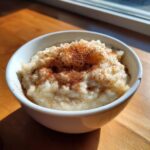 Close-up of a white bowl filled with creamy rice pudding recipe, generously dusted with cinnamon.