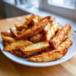 A close-up of a white plate piled high with golden brown, crispy air fryer potato wedges seasoned with paprika.