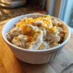 A white bowl filled with creamy crock pot chicken and rice topped with melted shredded cheddar cheese.