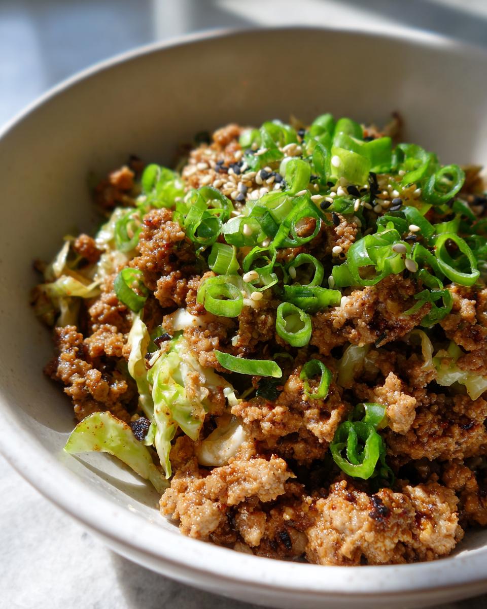Close-up of a hearty serving of egg roll in a bowl, featuring ground meat, cabbage, and topped with fresh green onions and sesame seeds.