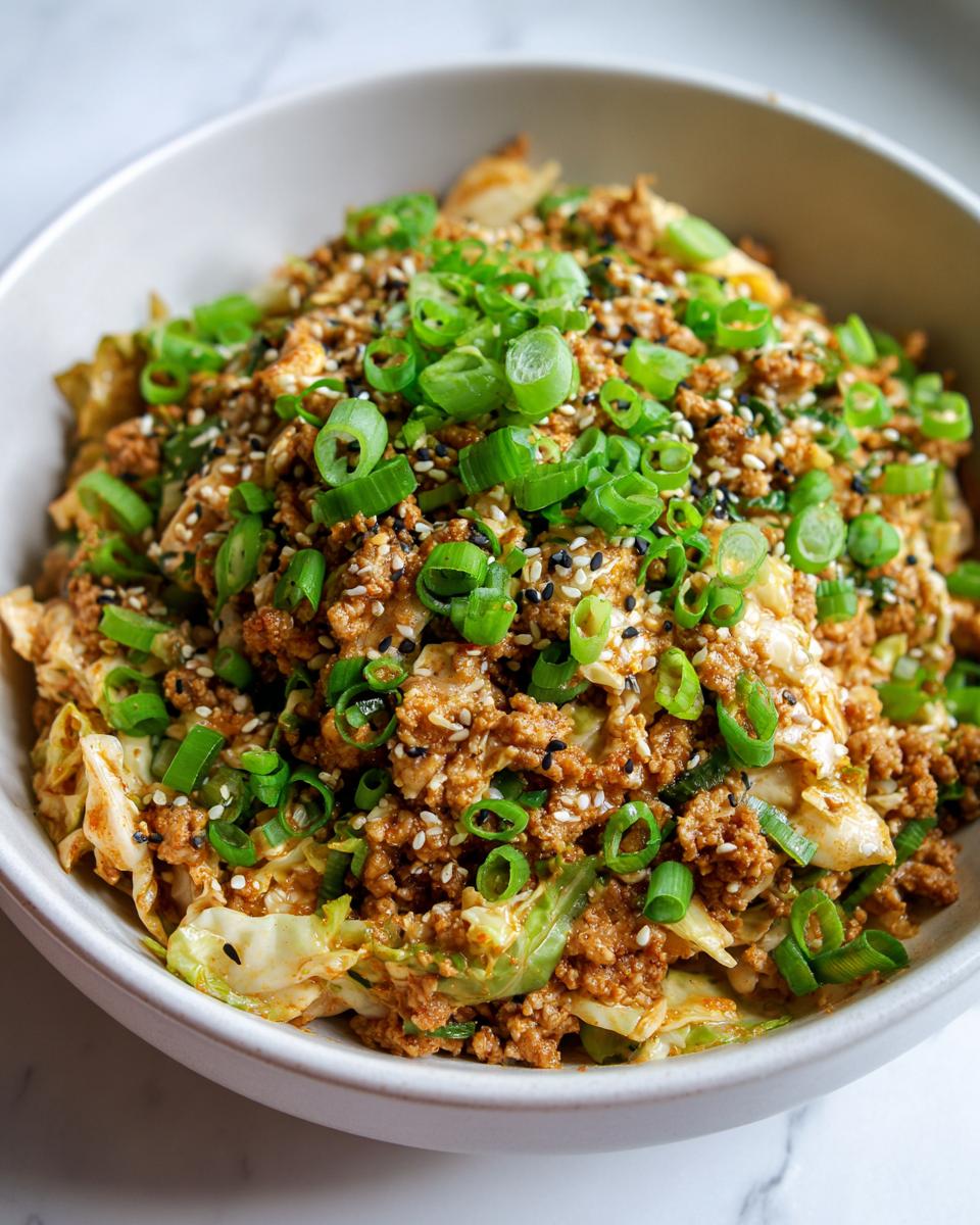 A close-up of a savory egg roll in a bowl mixture topped generously with sliced green onions and sesame seeds.
