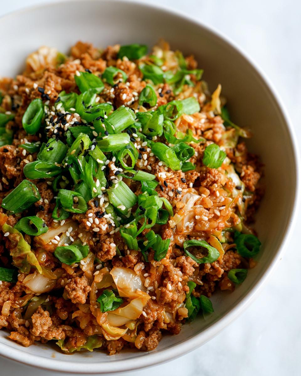 A close-up view of a bowl filled with savory egg roll in a bowl mixture, topped with fresh green onions and sesame seeds.