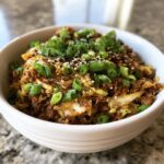 Close-up of a white bowl filled with savory egg roll in a bowl mixture topped with green onions and sesame seeds.