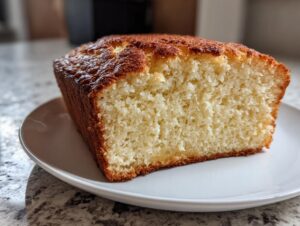 A thick slice of golden-brown beer bread showing its fluffy, light interior texture on a white plate.