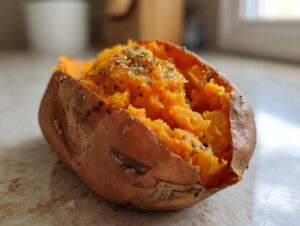A close-up of a fluffy baked sweet potatoes, split open and topped with herbs and spices.