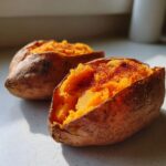 Two fluffy baked sweet potatoes split open and seasoned, showing bright orange flesh.