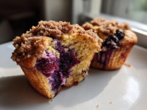 Close-up of a fluffy blueberry muffin cut in half showing moist interior and burst blueberries, topped with cinnamon streusel.